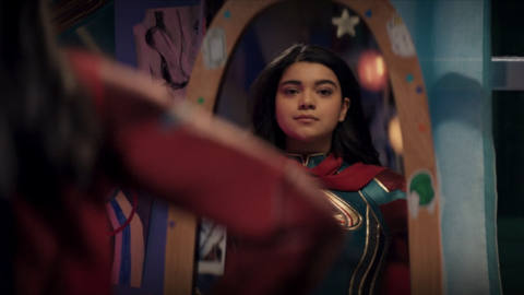 Kamala Khan/Ms. Marvel looks at herself in the mirror, smiling quietly and proudly at her superhero duds in Ms. Marvel. 