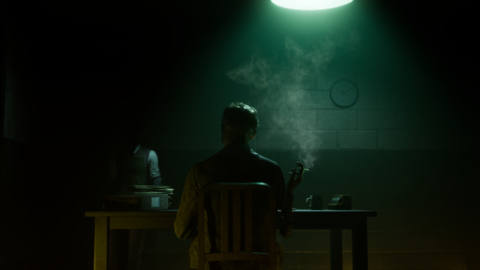 A dark figure is seen behind smoking at a desk in The Dark Pictures: The Devil in Me