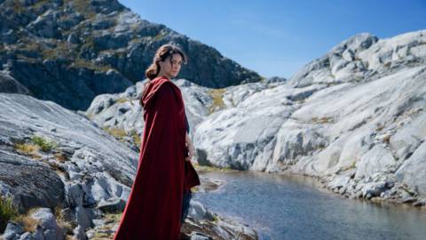 Nazanin Boniadi as Bronwyn stands by a river in a still from The Lord of the Rings: The Rings of Power