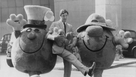 A black and white photo of Roger Hargreaves with Mr. Men characters in mascot costumes