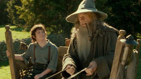 Frodo smiles like a goof while looking up at Gandalf who is steering the cart and smoking weed in The Lord of the Rings: Fellowship of the Rings