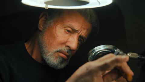 Sylvester Stallone closely examines an item through a mounted magnifying glass in Samaritan.