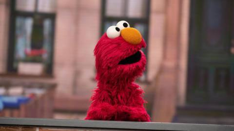 A photo of Elmo the puppet from Sesame Street on the Today Show. He is sitting behind a desk as he looks to the side. 