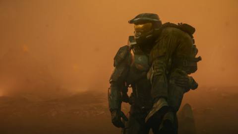 Master Chief (Pablo Schreiber) standing and holding a person slung over his shoulder