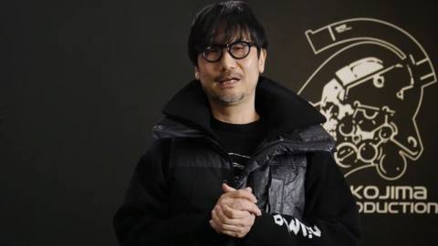Hideo Kojima stands in front of the Kojima Productions logo in a video promoting the game PHYSINT