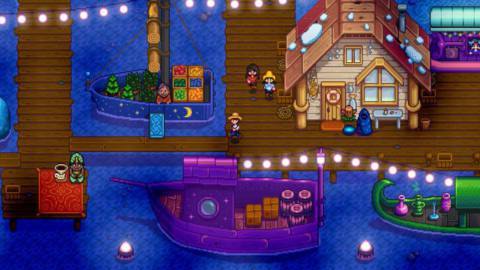 The Night Market, a collection of boats with wares to trade and sell that have gathered in the docks in Stardew Valley. The sky is dark, and the scene is illuminated by lights strung along the pier.