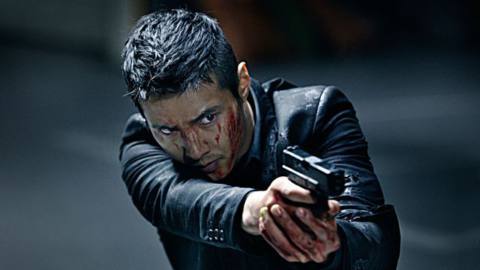 A man in a black suit (Won Bin) with blood on his face and hands trains the sights of a pistol at an off-screen target.