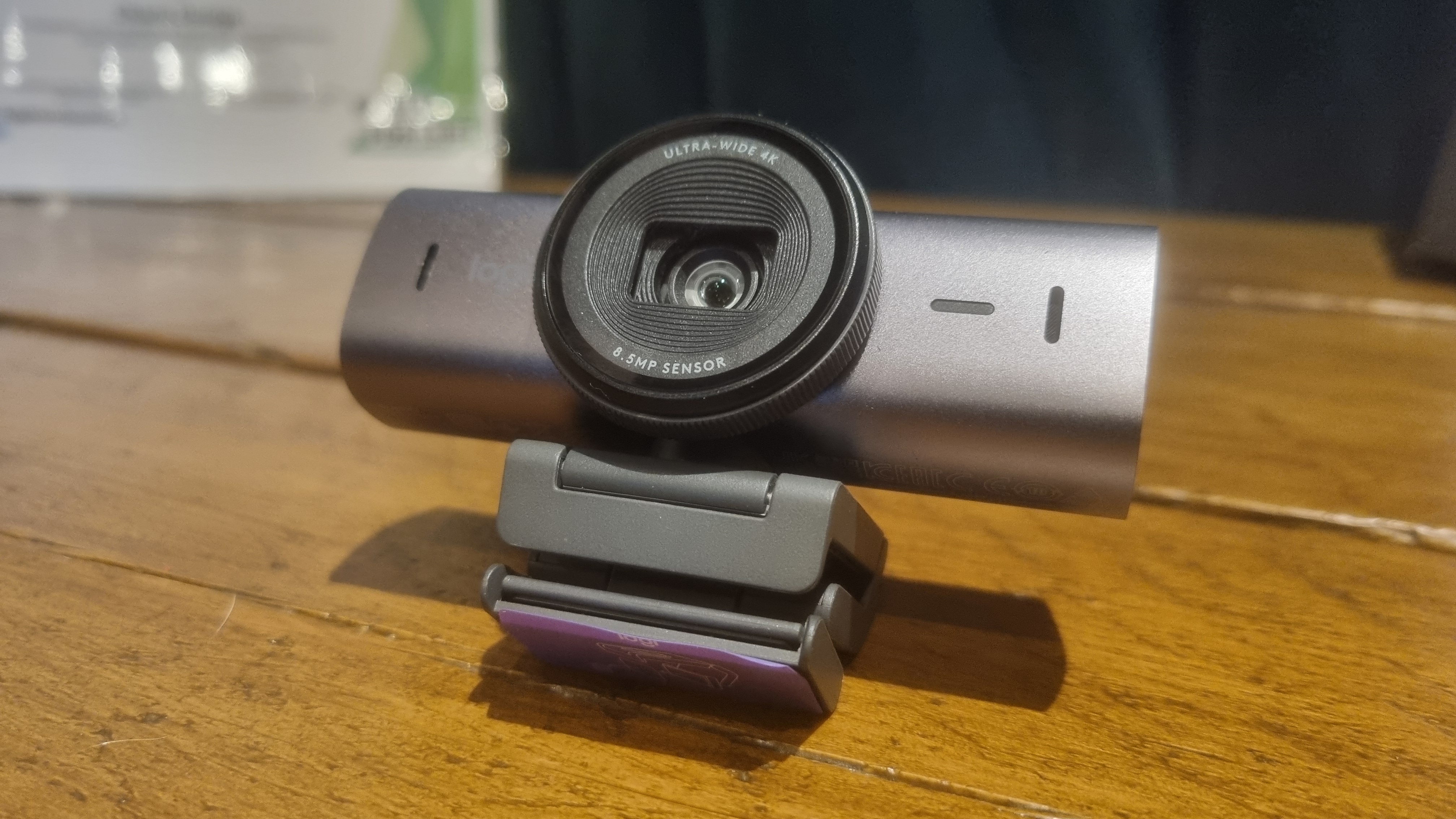 The Logitech MX Brio webcam attached ot its stand, folded up on a wooden table