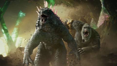 Godzilla, now with pink spikes on his back, roars as King Kong, now with a robot hand, roars up behind him as they stand in a cavern together in Godzilla x Kong: The New Empire
