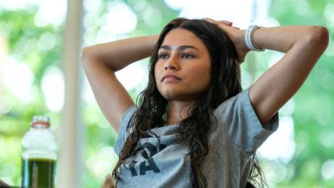 Teenage tennis prodigy Tashi (Zendaya), in a loose blue T-shirt, sits in a school cafeteria with her hands behind her head and looks contemplative in Luca Guadagnino’s Challengers