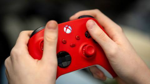 A close-up of a child’s hands holding a red Microsoft Xbox controller