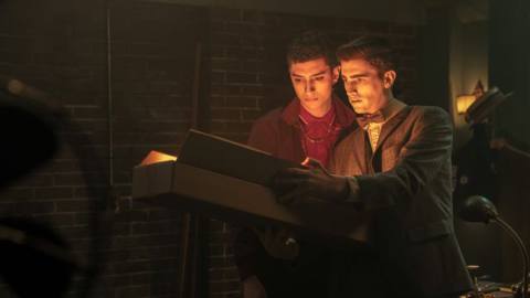 (L to R) Jayden Revri as Charles Rowland and George Rexstrew as Edwin Payne in Dead Boy Detectives. They’re opening a big box, with a light from within illuminating their faces. 