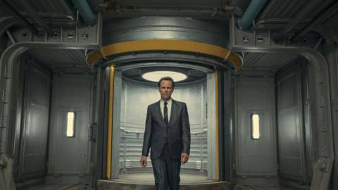 A still of Walton Goggins walking out of a Vault door in a suit, talking to the camera