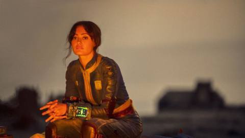 Lucy (Ella Purnell) sitting by a fire looking solemn in a still from Fallout