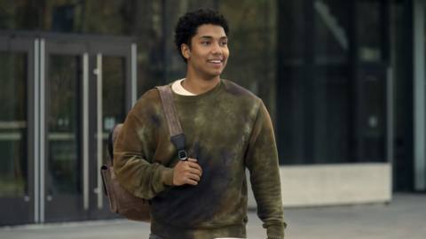 Godolkin student Andre (Chance Perdomo) cheerily walks out of a building with a bag hanging off his shoulder, unaware of the horrors that await him in the Prime Video series Gen V.