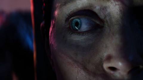 An extreme close-up of Hellblade 2’s Senua glancing to her right - in the background is another figure, out of focus