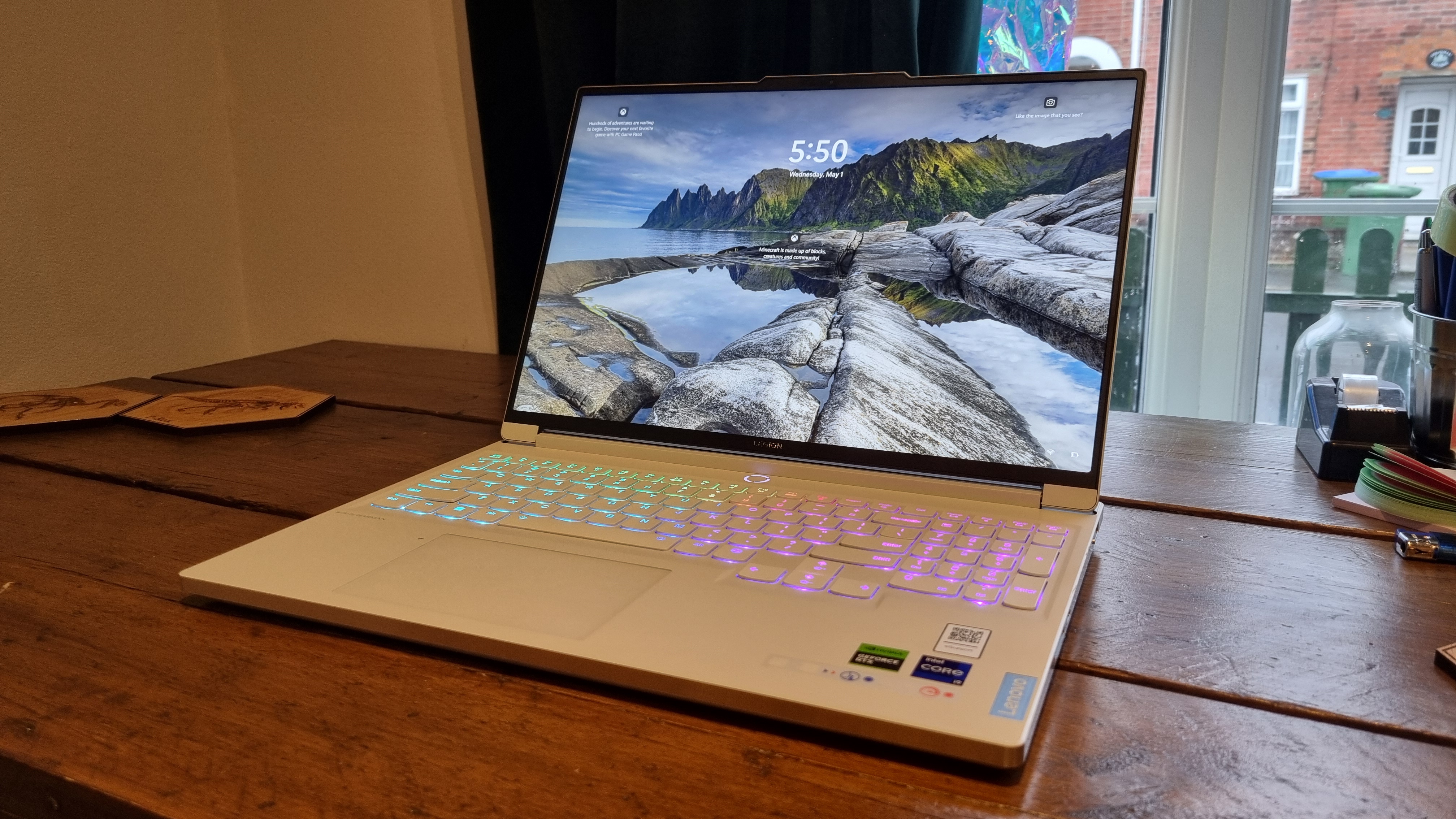 The Lenovo Legion 7 16IRX9 sitting on a wooden table, open, with keyboard showing rainbow RGB colours