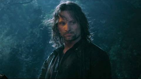 A bedraggled Aragorn stands in a forest, holding a lit torch in The Fellowship of the Ring.