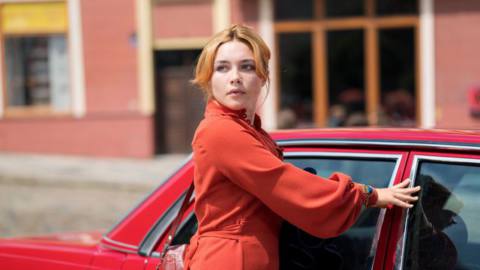 Florence Pugh, wearing red, closes the door of a red car in The Little Drummer Girl.