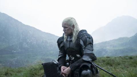 Daemon (Matt Smith) in full armor and his long white hair sitting on a grassy hill with fog behind him in House of the Dragon season 2