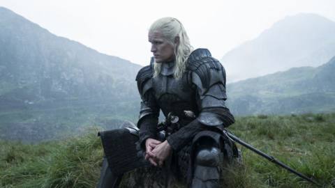 Daemon (Matt Smith) in full armor and his long white hair sitting on a grassy hill with fog behind him in House of the Dragon season 2