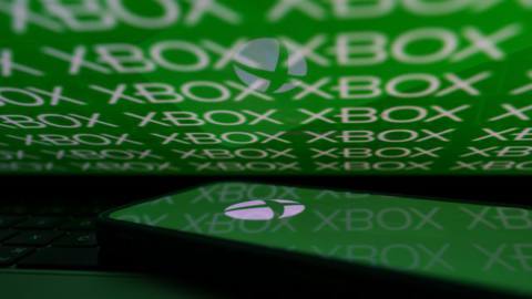 In this photo illustration, the Xbox logo is displayed on a mobile phone screen in front of a laptop screen that is also displaying the logo