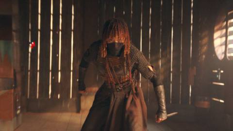 Mae&nbsp;(Amandla Stenberg) in The Acolyte. She’s standing in a fighting stance in a wooden-slatted building, a small dagger gripped in one hand. The bottom of her face is covered by a cloth mask.