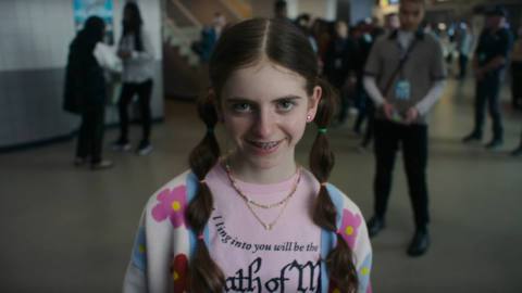 A little girl looks toward the camera while walking toward it with an unnatural grin on her face in Smile 2 