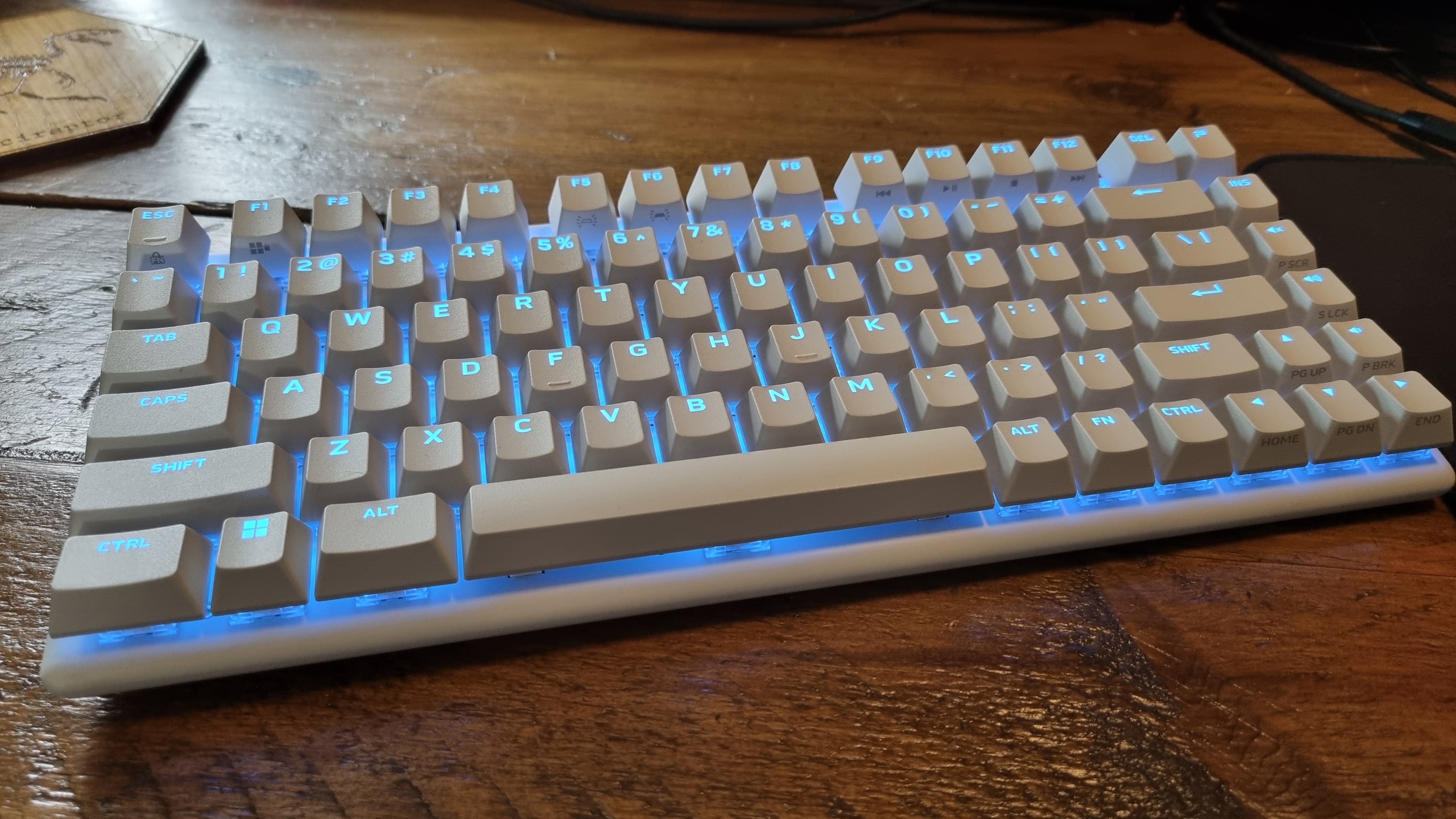 The Alienware Pro Wireless Gaming Keyboard, lit up in blue on a wooden desk
