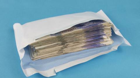 A Getty photo of a plain white envelope packed with UK £20 notes against a blue background