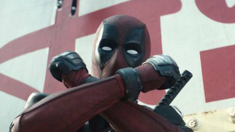 Deadpool (Ryan Reynolds, in costume) stands on a billboard catwalk, making the X-Force crossed-wrists gesture in Deadpool 2