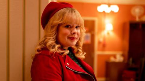 Nicola Coughlan, wearing a red beret and matching red suede jacket, smiles into the camera in Doctor Who Christmas special Joy to the World
