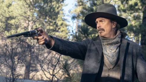 A man with a moustache in a dark grey hat and jacket aiming a revolver in a forest in Horizon: An American Saga - Part 1.