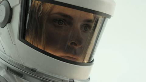 Rebecca Ferguson as Juliette in Silo season 2, wearing a white environmental suit and standing somewhere with a bright light behind her