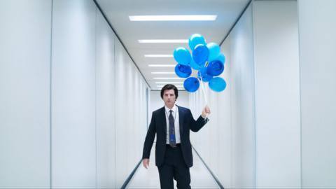 Mark (Adam Scott) standing in a hallway of Lumon Industries with balloons