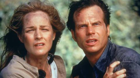 Helen Hunt and Bill Paxton hold on to each other muddied by a storm as they brace for something off screen in a scene from Twister.