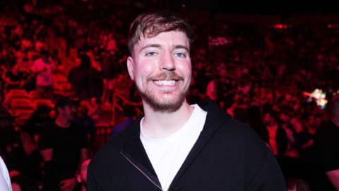 A photograph of Jimmy Donaldson, aka MrBeast, smiling at the camera. A huge crowd of people is behind him