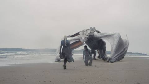 Rhaenyra walks towards Alyn kneeling on a beach in front of his dragon