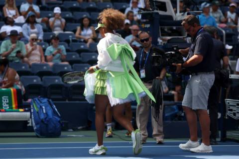 Naomi Osaka of Japan walks onto the tennis court on day two of the 2024 US Open in a frilly lime-green skirt, white jacket, and big green bow in the center of her back