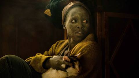 Sam (Lupita Nyong’o) sits fearfully in a dark space, covered with dust, her cat Frodo in her lap, in Michael Sarnoski’s A Quiet Place: Day One