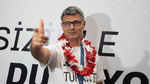 A photo of the Turkish Olympic silver medalist shooter Dikec after he returned home. He is pointing his finger like a gun. 