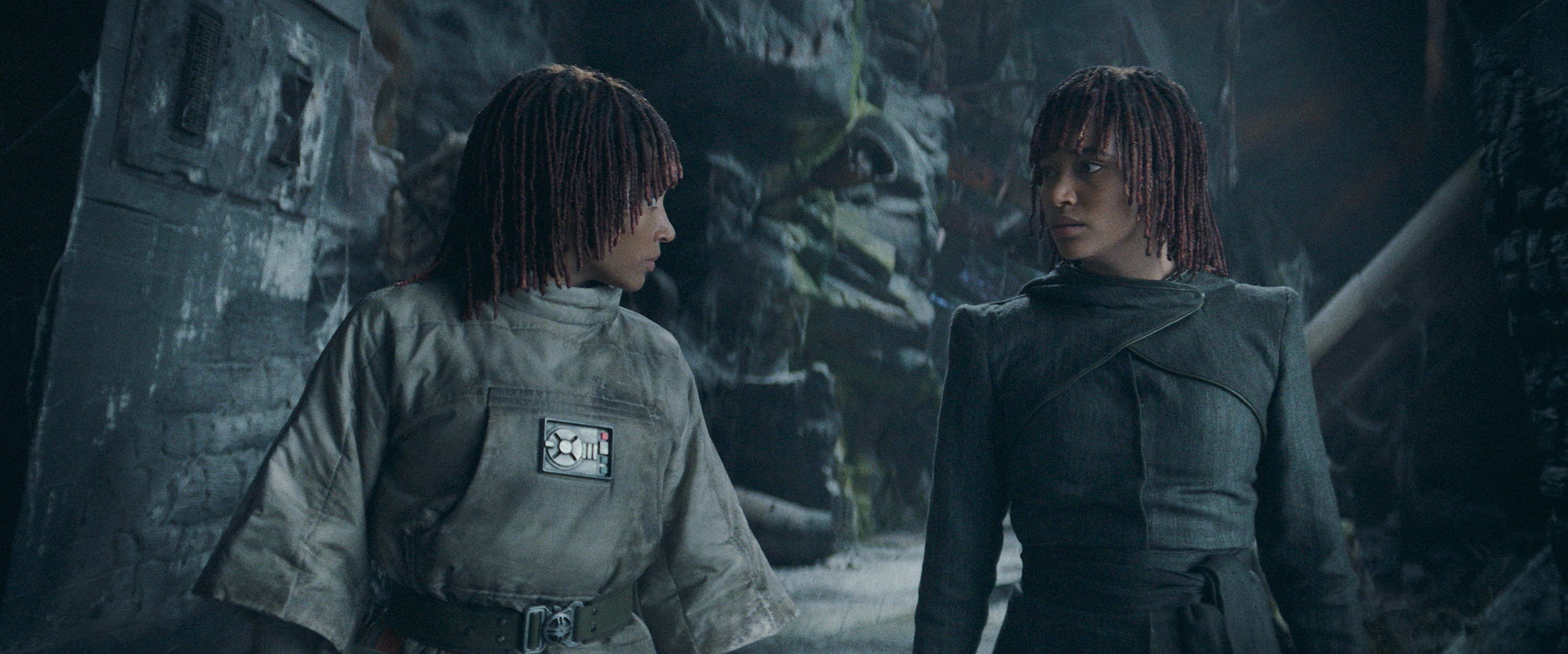 Twin sisters Mae and Osha (both played by Amandla Stenberg) stand in a rough-hewn rock corridor filled with wreckage and stare at each other in the Star Wars TV series The Acolyte