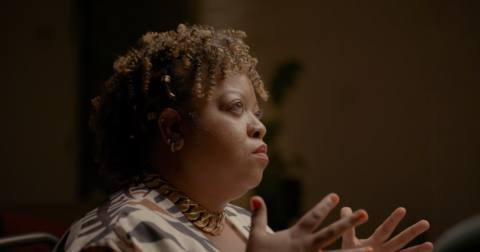 A middle-aged Black woman raises her hands during a psychic reading in Look Into My Eyes