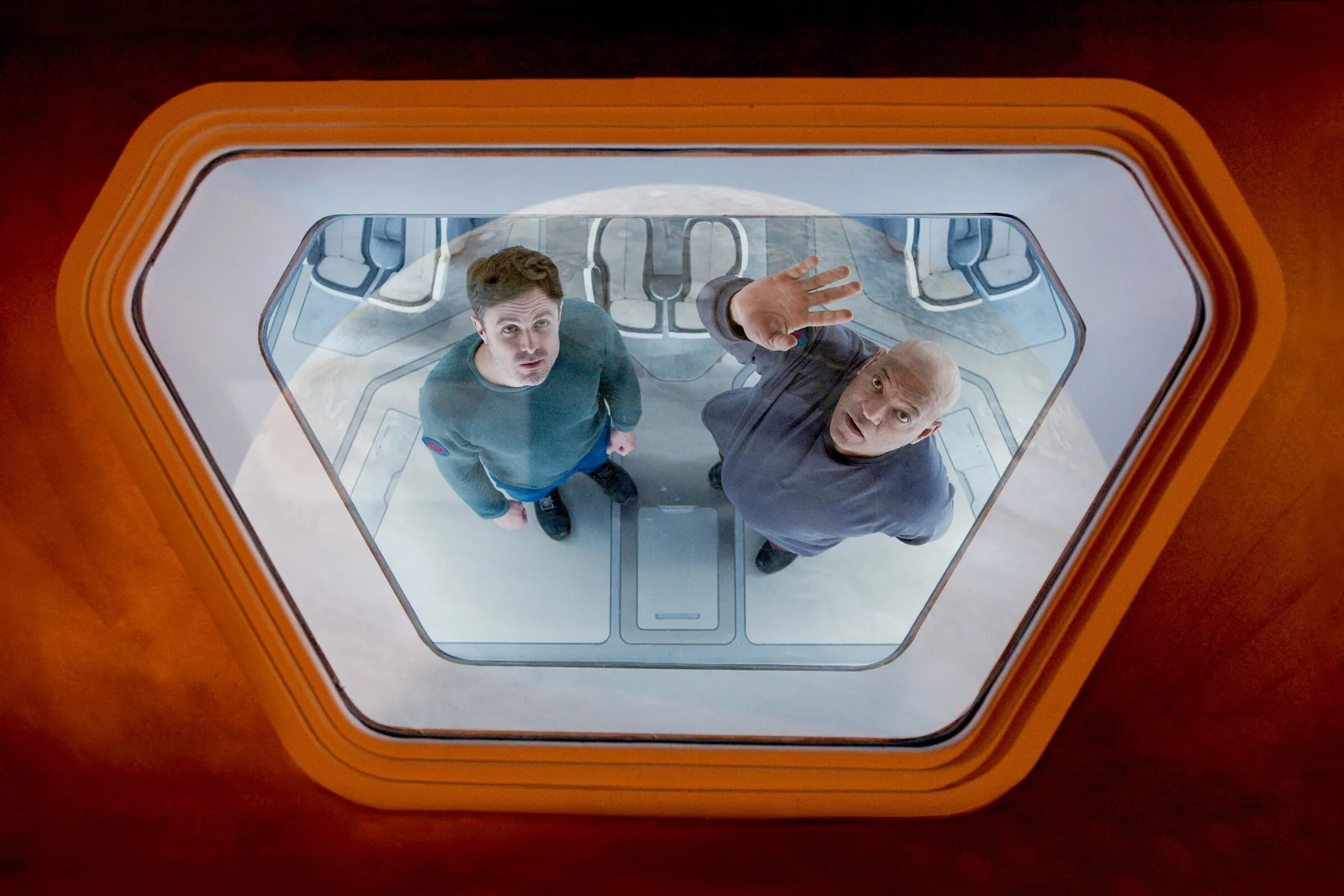 Casey Affleck and Laurence Fishburne staring up through the porthole of a spaceship at a nearby planet in Slingshot.