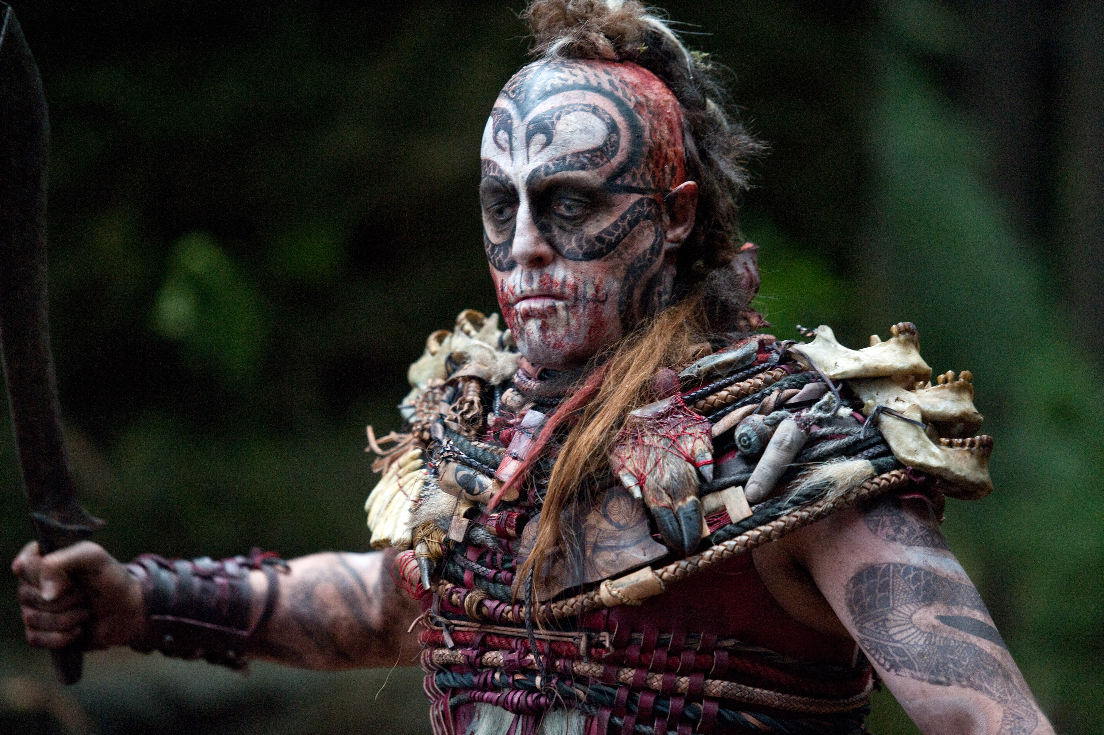 Hugh Grant in one of his many Cloud Atlas roles, as a cannibal chieftain with a shaved head and topknot; red, white, and black tattoos of stylized snakes all over his face and arms, and clothing consisting of braided leather decorated with bones and animal and human body parts