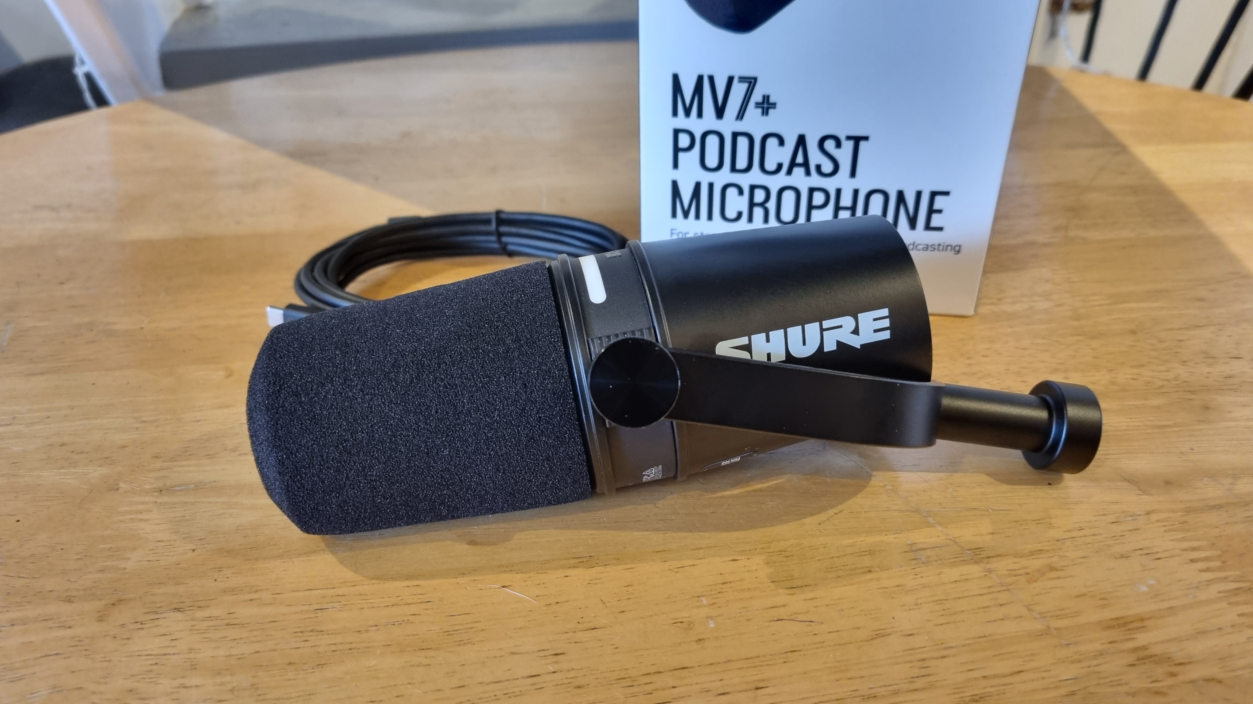 The Shure MV7 Plus microphone on a table, with the box behind