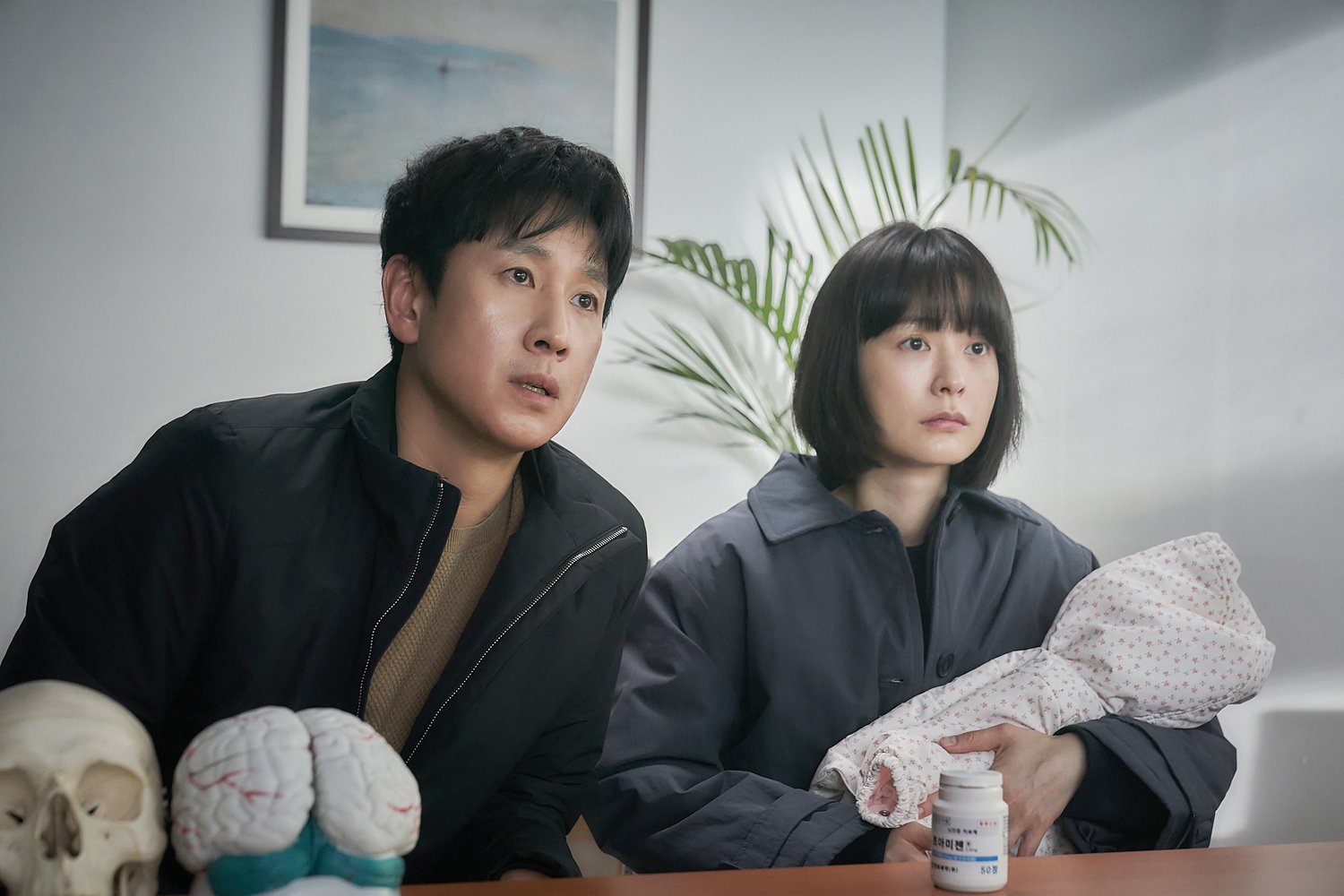 Soo-jin (Jung Yu-mi) and Hyun-su (Lee Sun-kyun) sit in a sleep doctor’s office, while Soo-jin holds a wrapped-up baby