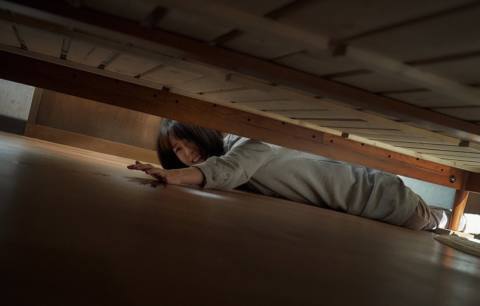 A woman reaches for something under the bed while looking very scared in Sleep