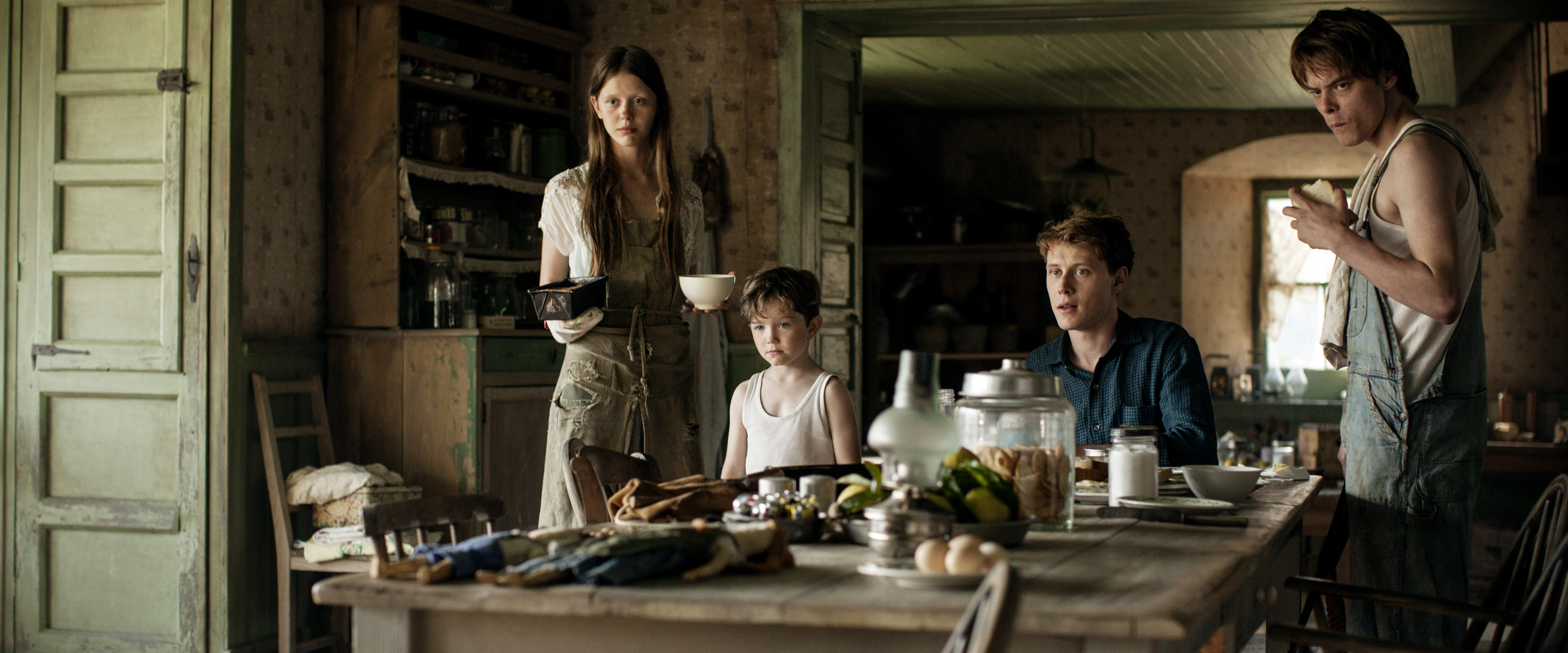 George MacKay, Mia Goth, and Charlie Heaton sit around a table in Marrowbone