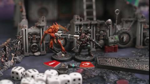 Two miniatures from Warhammer 40,000: Kill Team - Hivestorm facing off. One is a heavily armored member of the Imperial Guard (right); the other is one of the Tau’s Vespid Stingwings (left). There are dice and game tokens in the foreground of the image